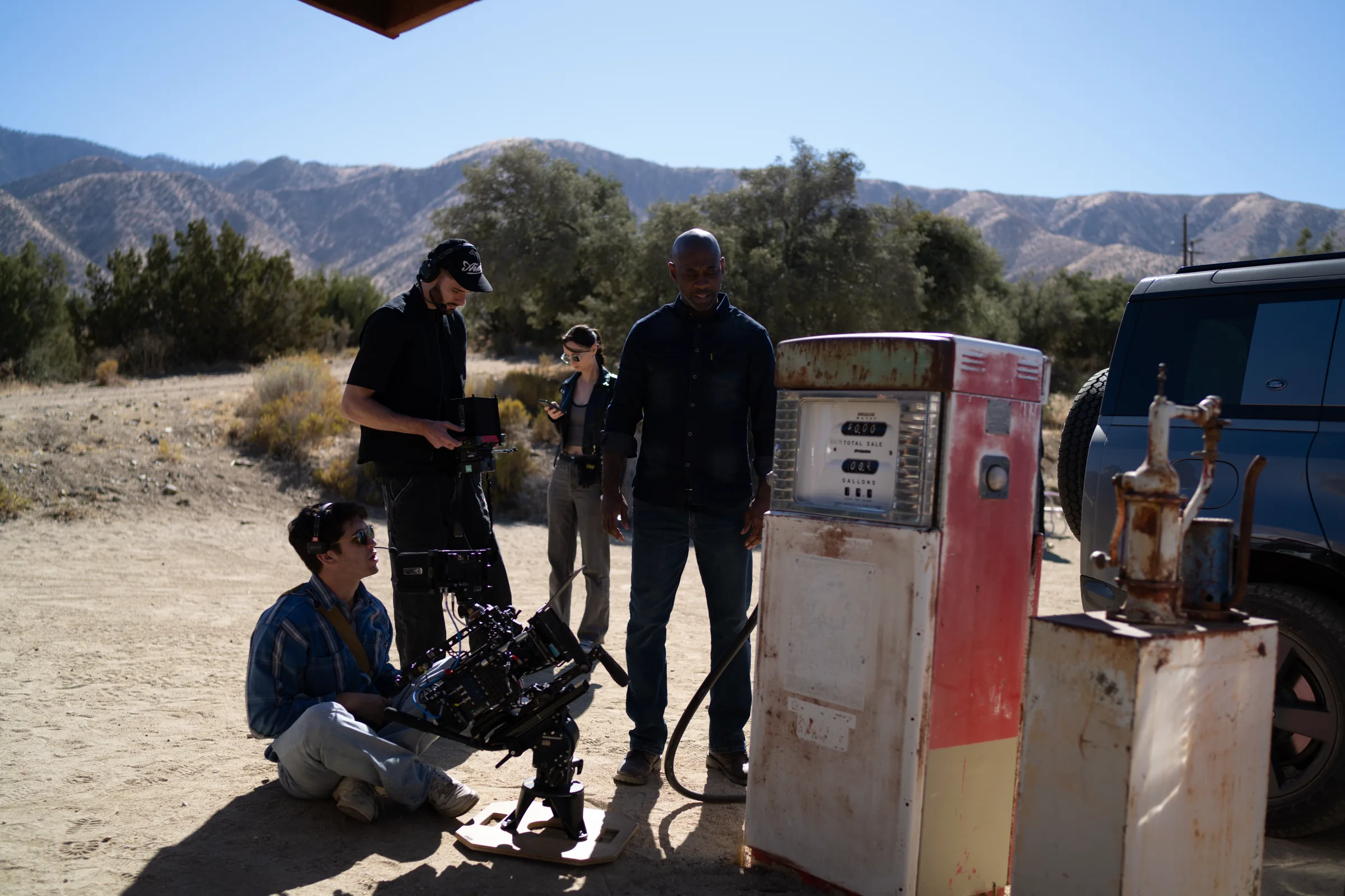 Crew with a rigged cinema camera and talent beside a rusty vintage gas pump in the desert