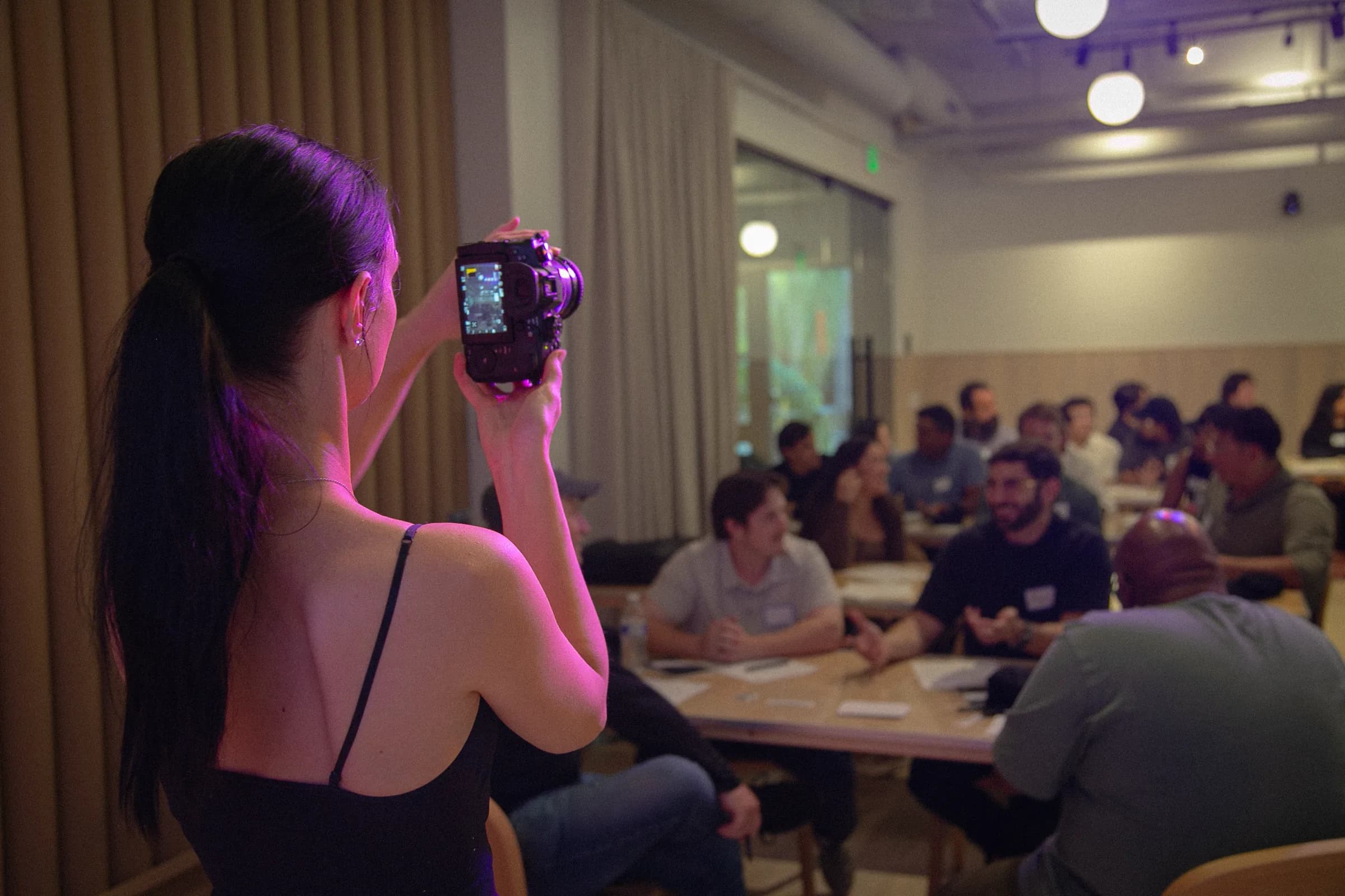 Photographer in purple light capturing a workshop, with attendees at tables