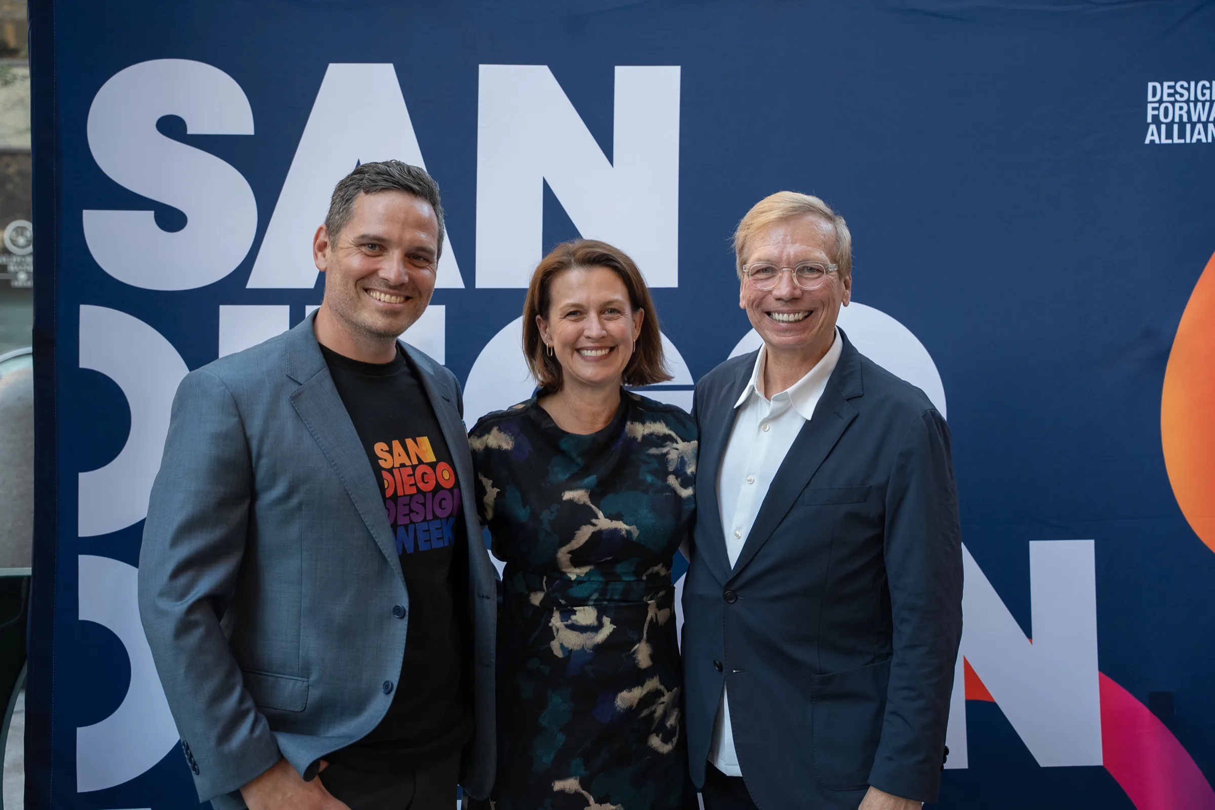 Three guests smiling in front of the San Diego Design Week backdrop, with the Design Forward Alliance mark at the top right